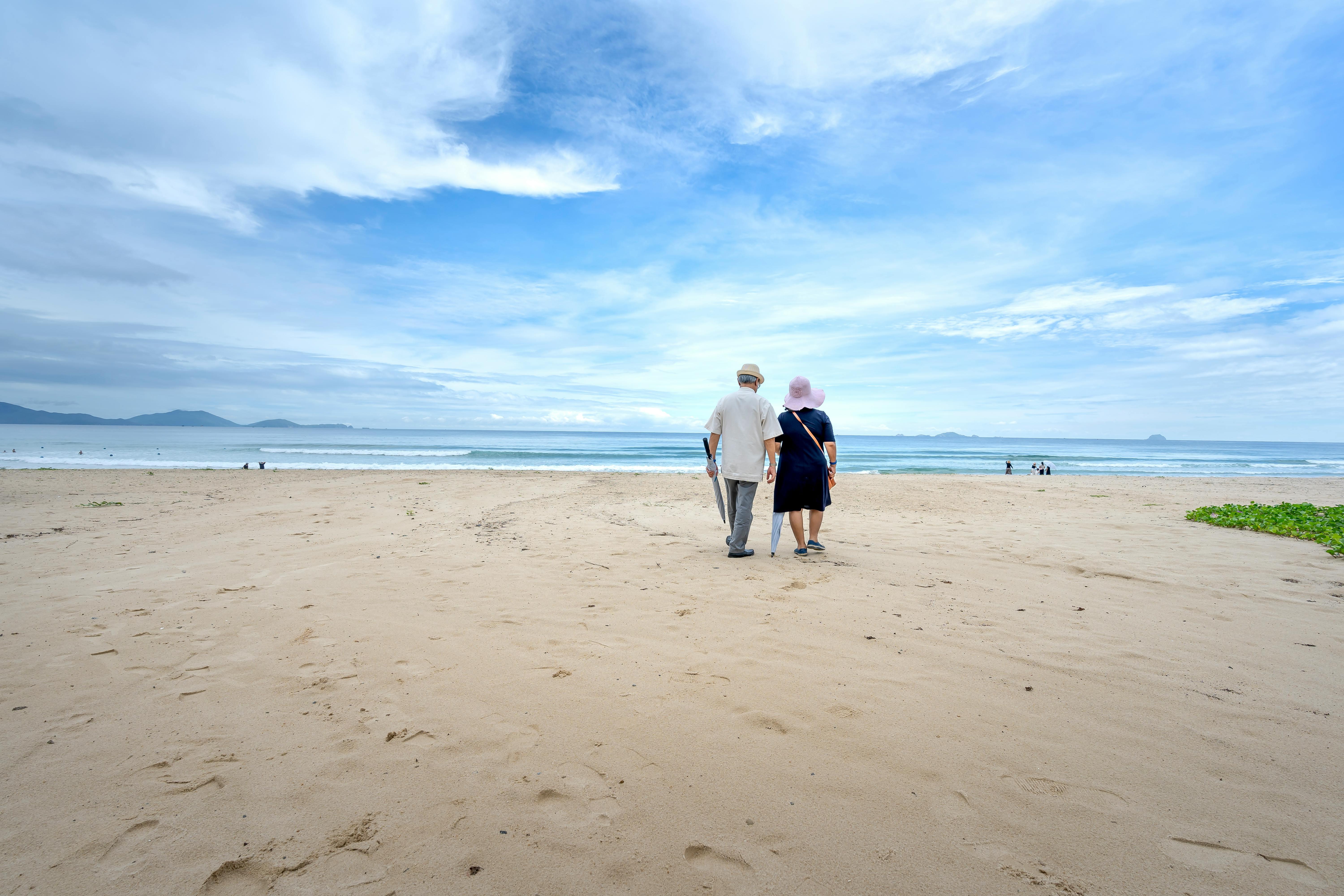 A couple walking together on a beach, looking out toward the ocean and distant mountains