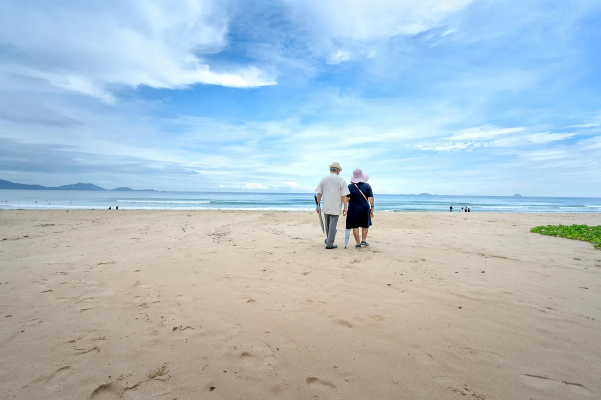 A couple walking together on a beach, looking out toward the ocean and distant mountains