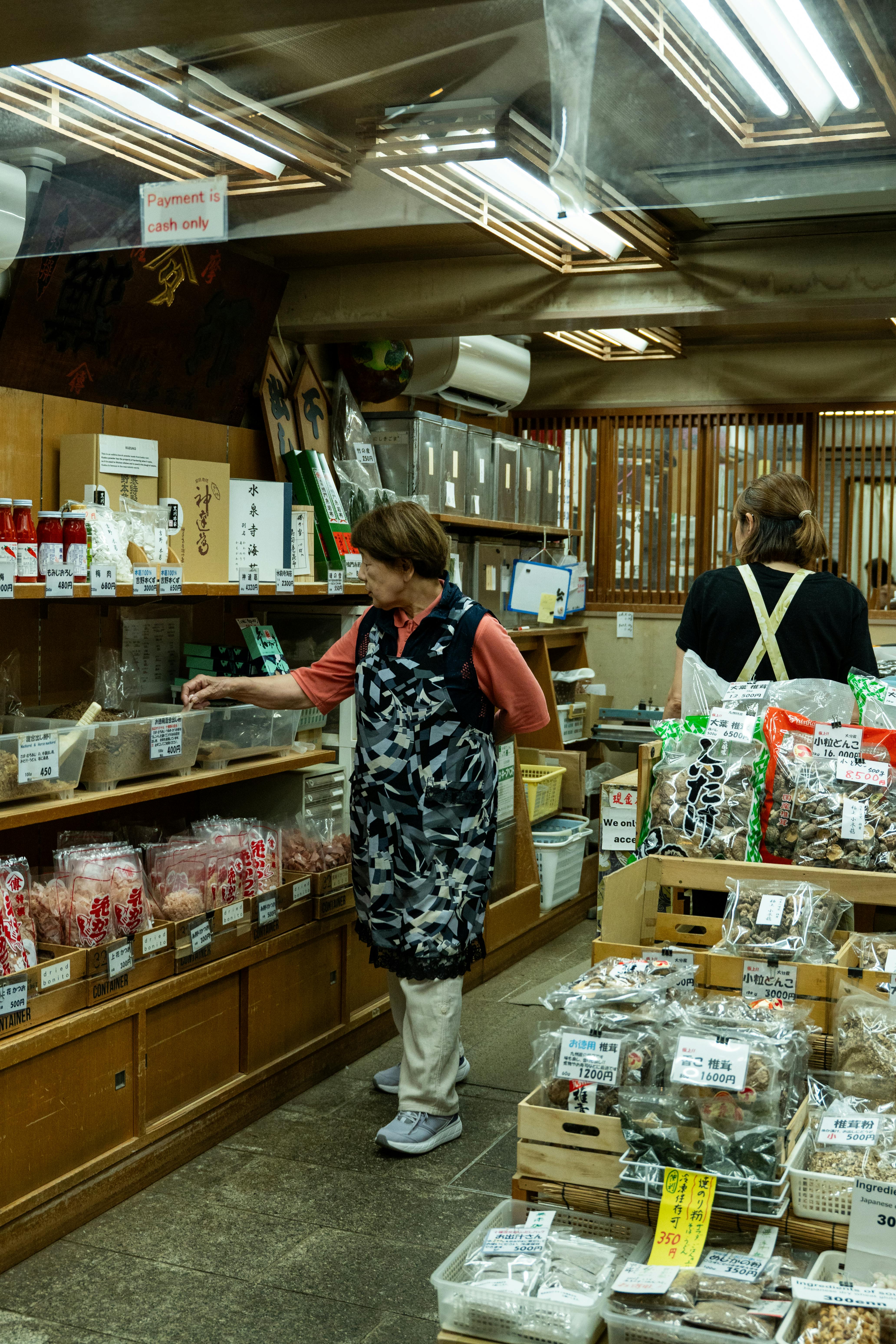 An elderly Japanese woman selecting traditional dried goods at a local market