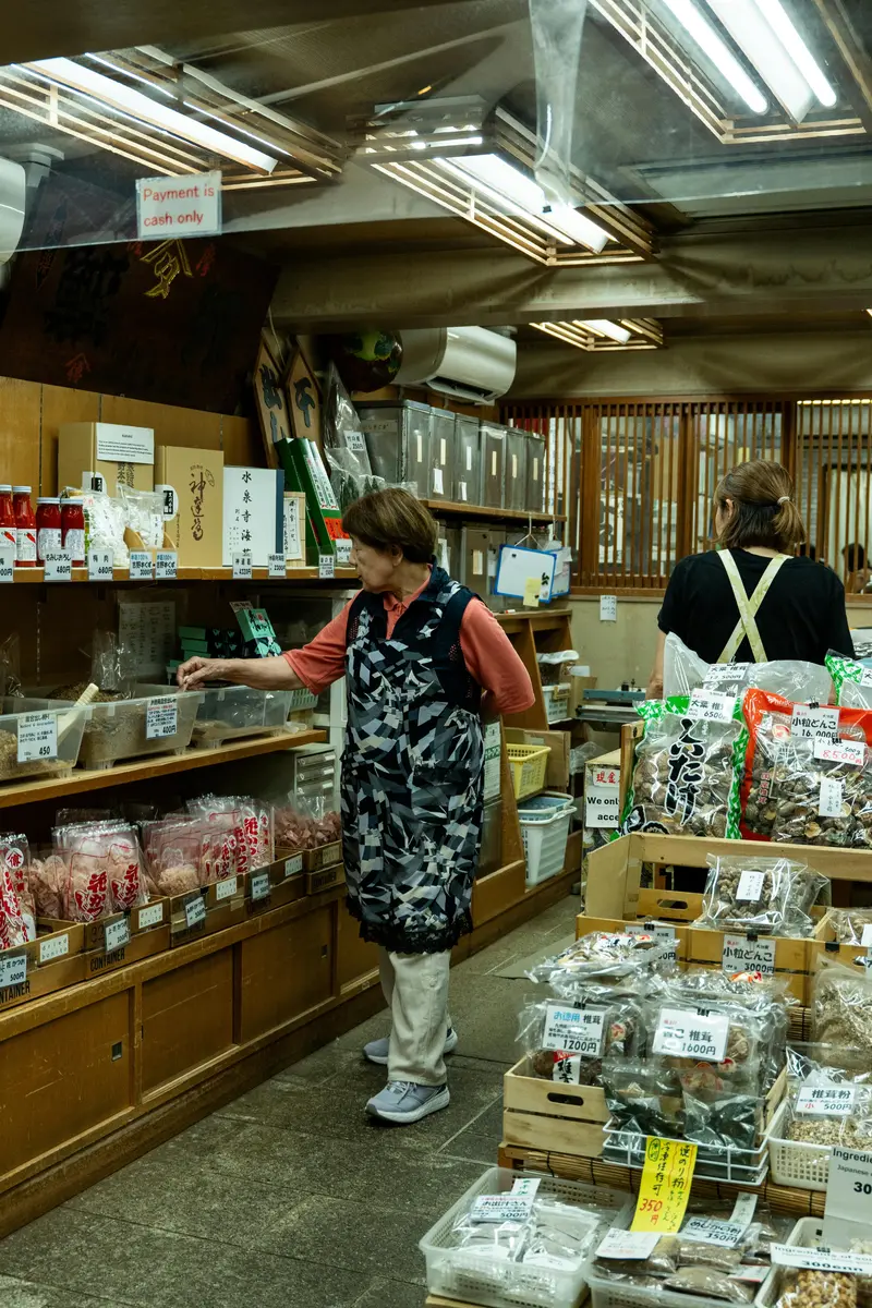 An elderly Japanese woman selecting traditional dried goods at a local market