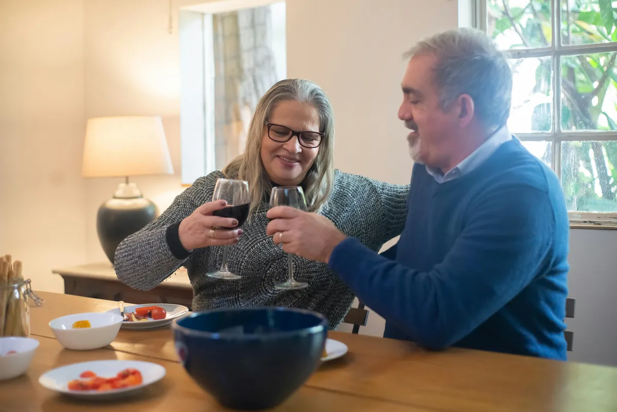 A couple sharing a toast with wine glasses over dinner at home, smiling warmly